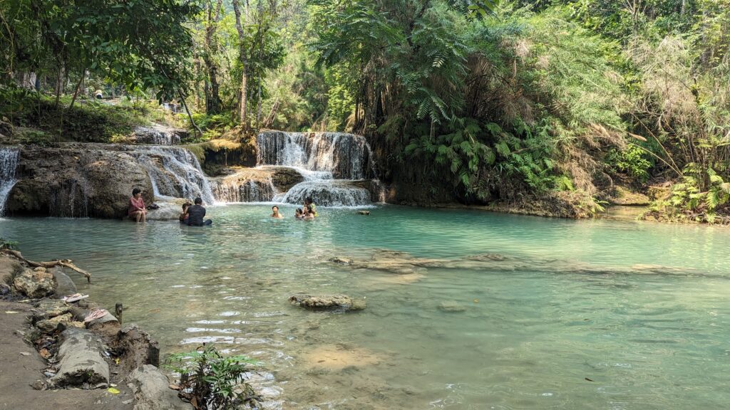 locals swiming in rockpool below waterfall at kuang si falls